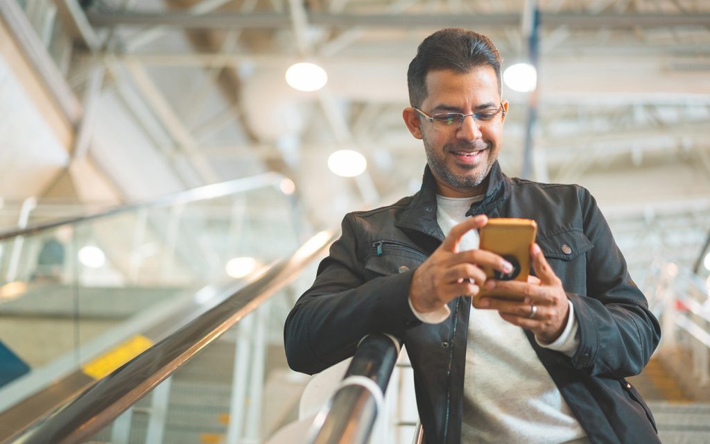 Man smiling at his phone while riding an escalator