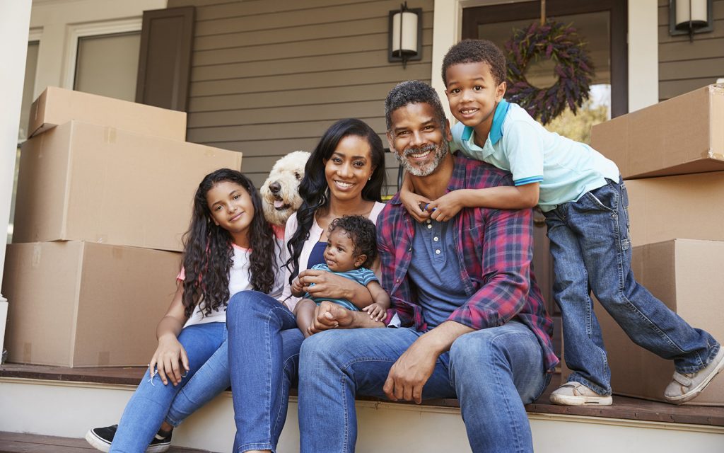 Family with children sitting among moving boxes on their front steps