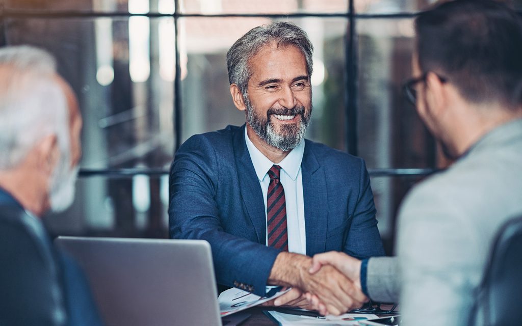 Two businessmen shaking hands over a laptop