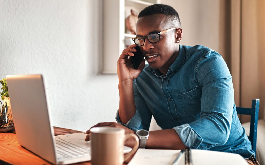 Man on a phone call working at a laptop with a coffee mug
