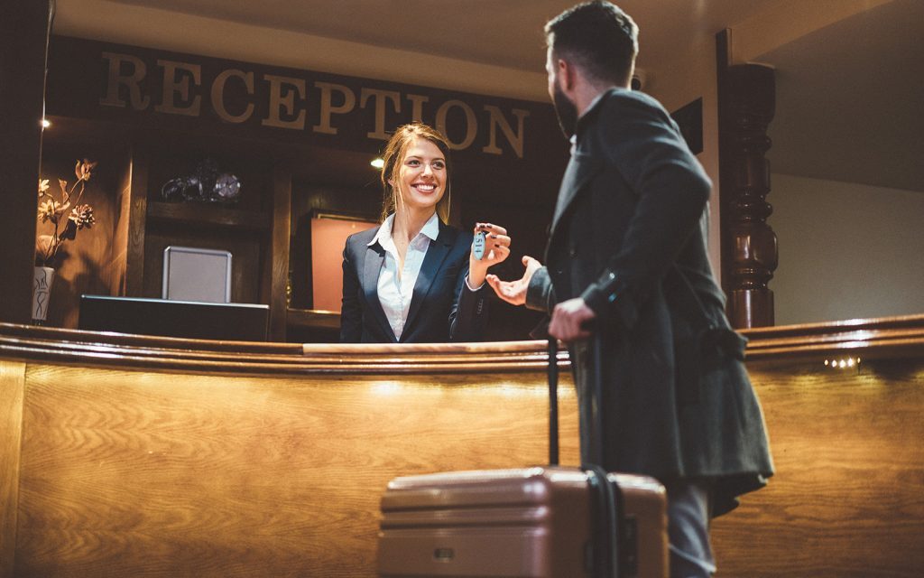 Hotel receptionist handing a key to a guest with luggage