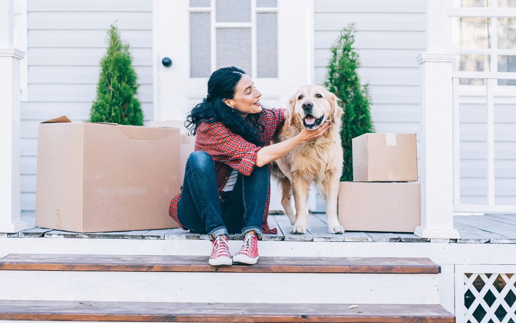 Woman sitting with her dog next to moving boxes on a porch