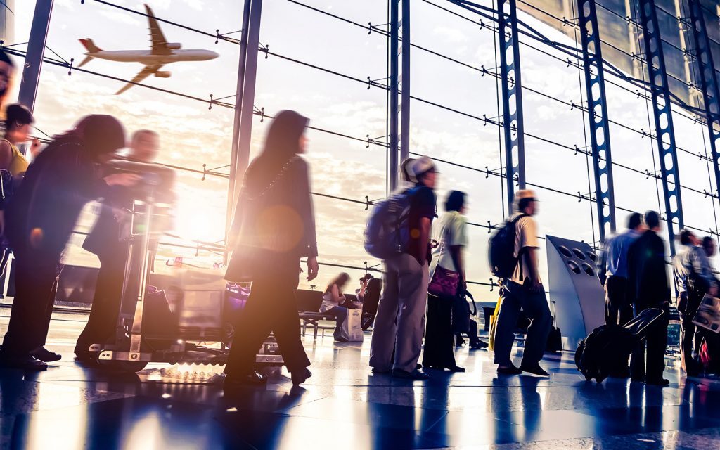 Travelers walking through an airport terminal as a plane takes off