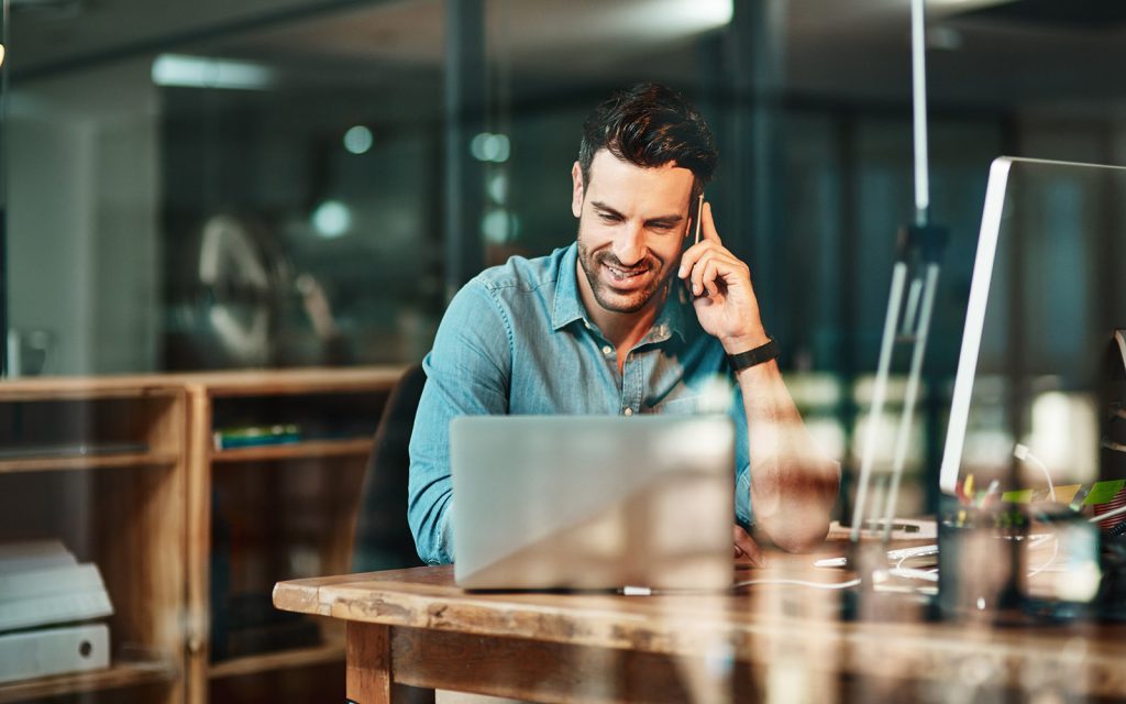 Man on the phone working at a laptop in an office