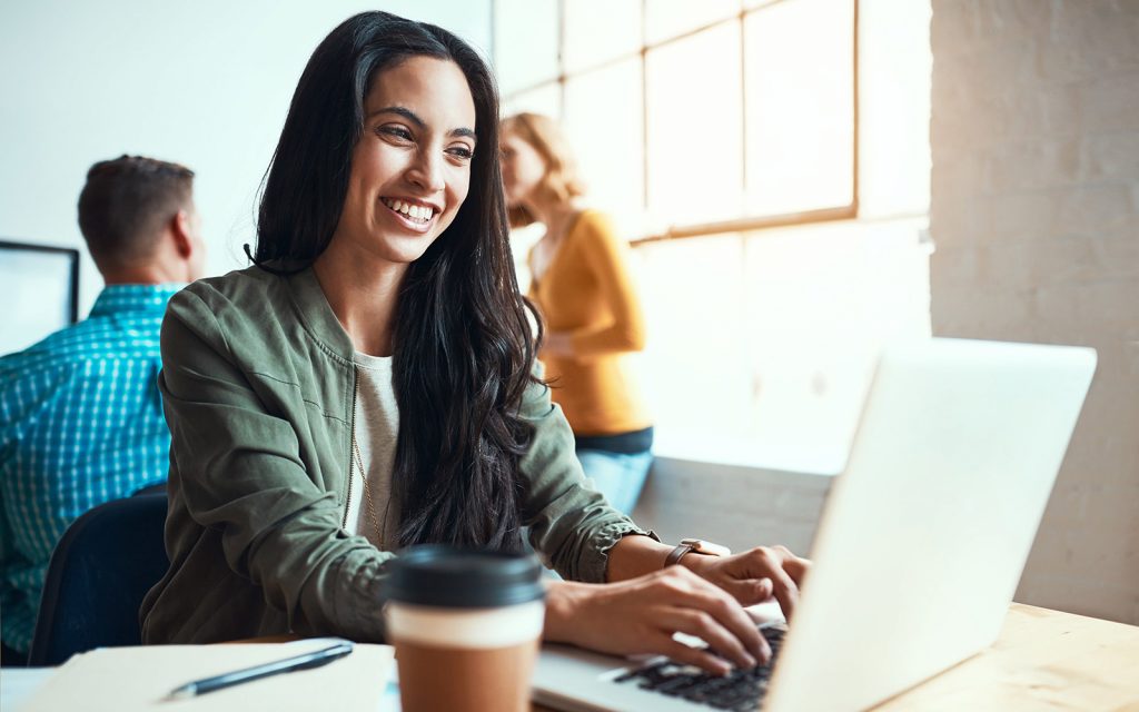 Smiling woman working on a laptop with a coffee beside her