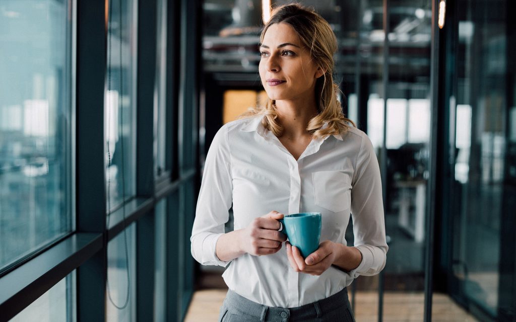 Woman holding a coffee mug looking out of an office window