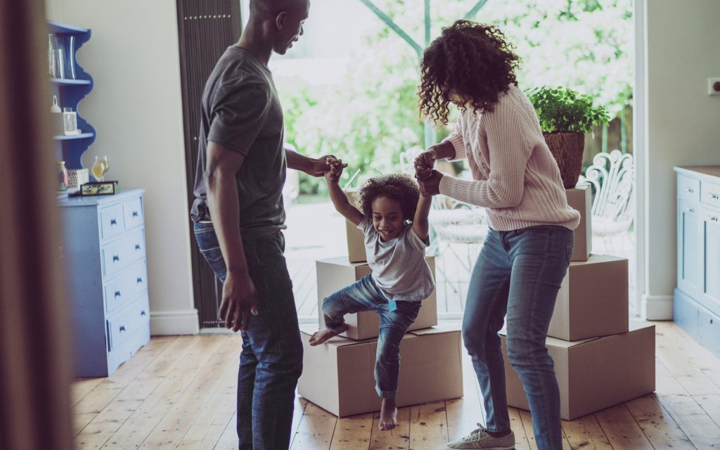 Parents lifting their young child among moving boxes in a new home