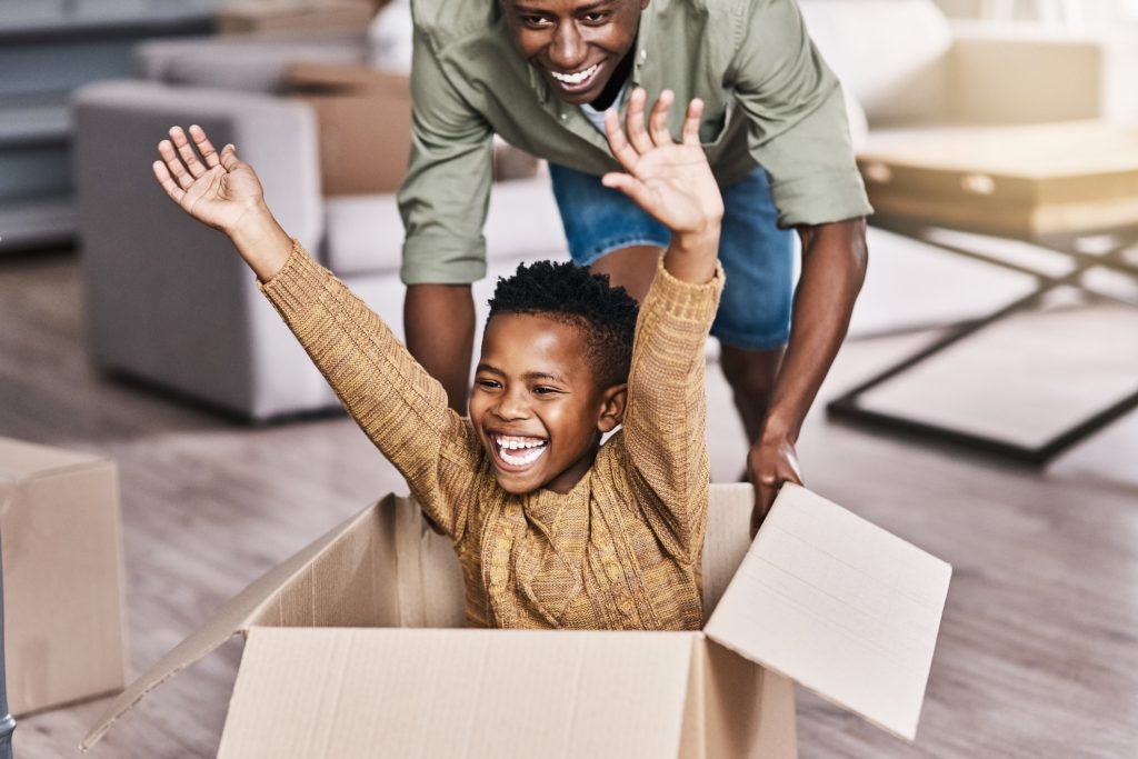 Child raising their arms in a moving box with a parent smiling behind