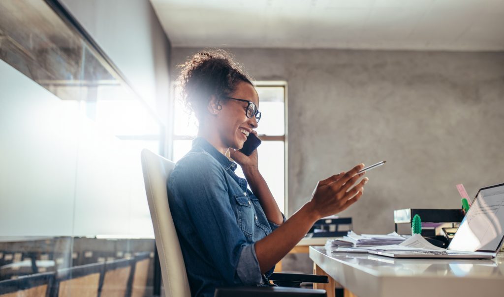 Woman on a phone call while using a tablet in a bright office
