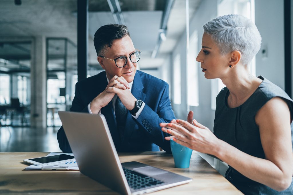 Two colleagues talking over a laptop in an office