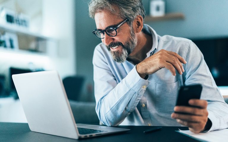 Man smiling while using his phone and laptop