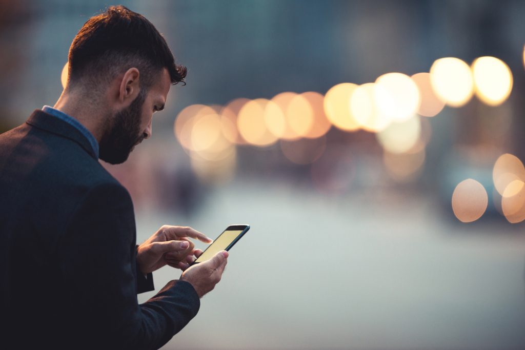 Man looking at his smartphone on a city street at dusk